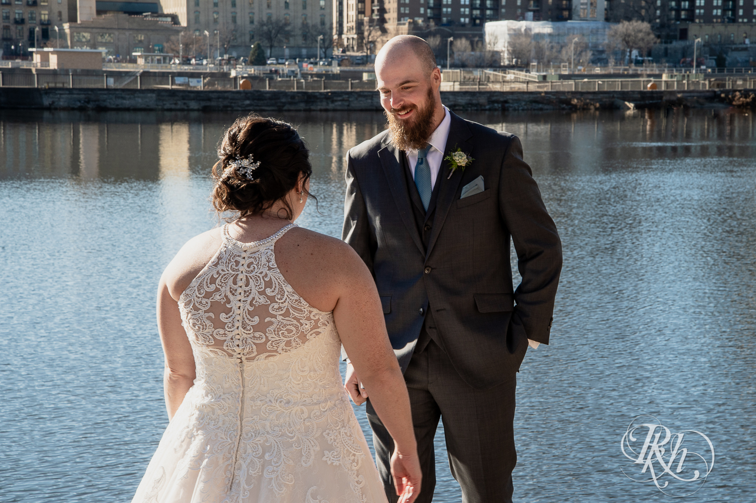 Bride and groom share first look at in front of river in Saint Anthony Main in Minneapolis, Minnesota.