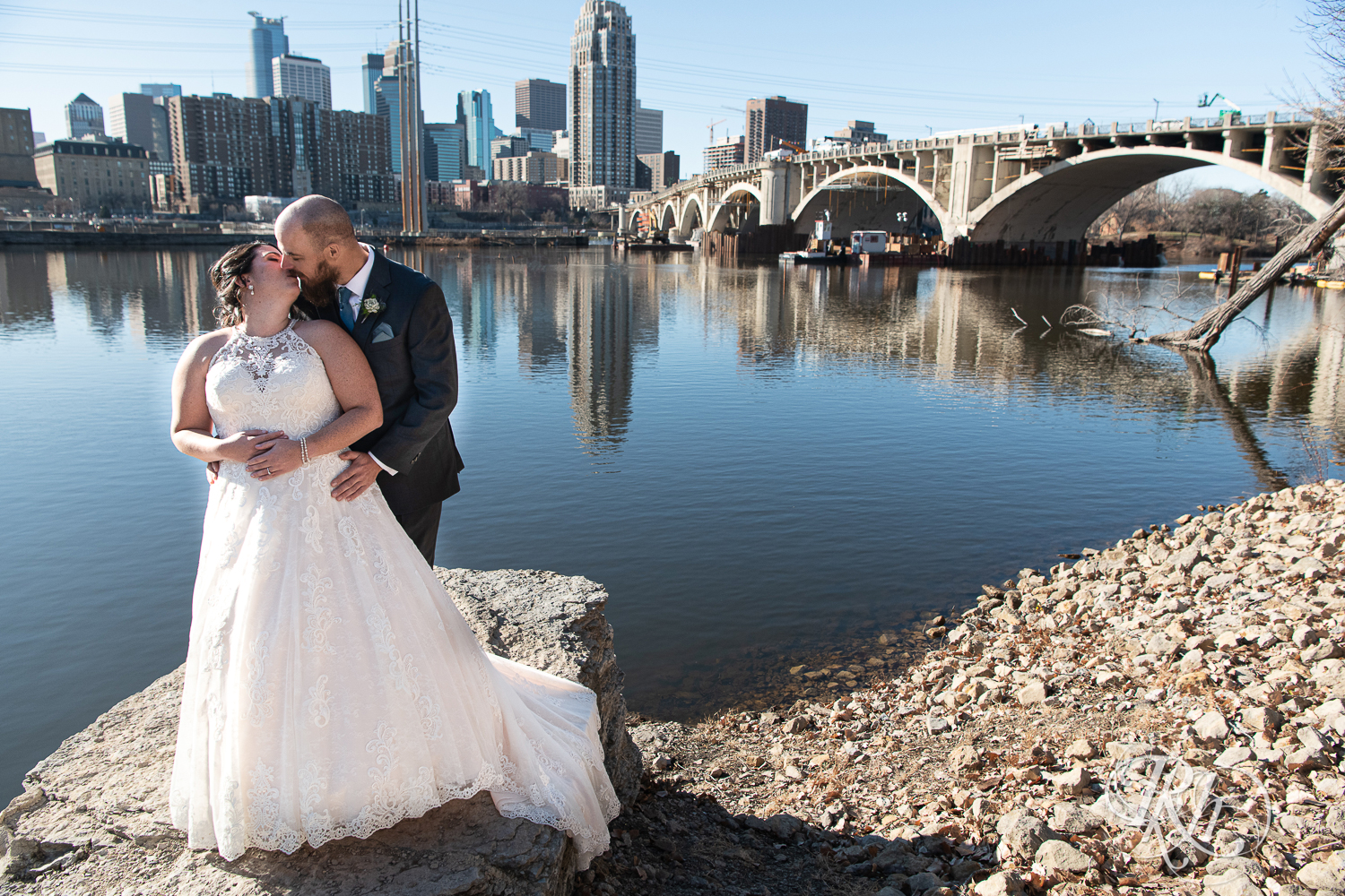 Bride and groom kiss in front of river in Saint Anthony Main in Minneapolis, Minnesota.
