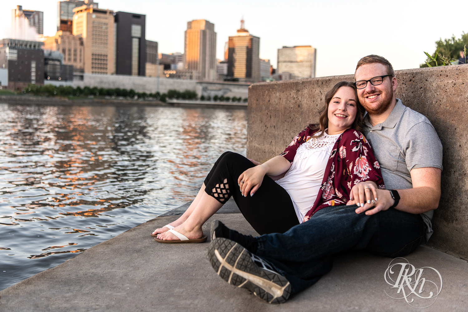 Man and woman smile with city in background during golden hour on Harriet Island in Saint Paul, Minnesota.