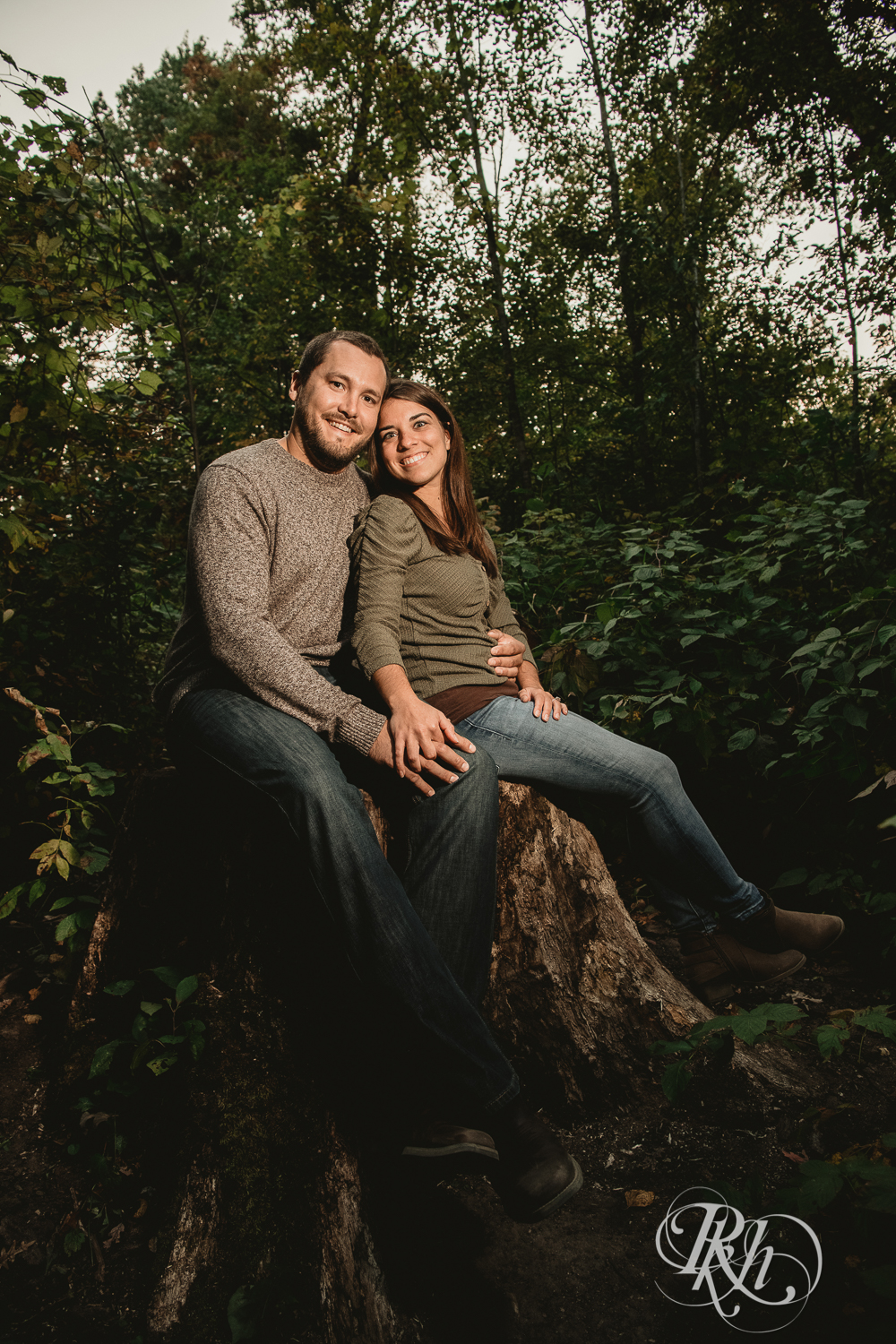 Man and woman in jeans and sweaters smile in woods at Lebanon Hills Regional Park in Eagan, Minnesota.