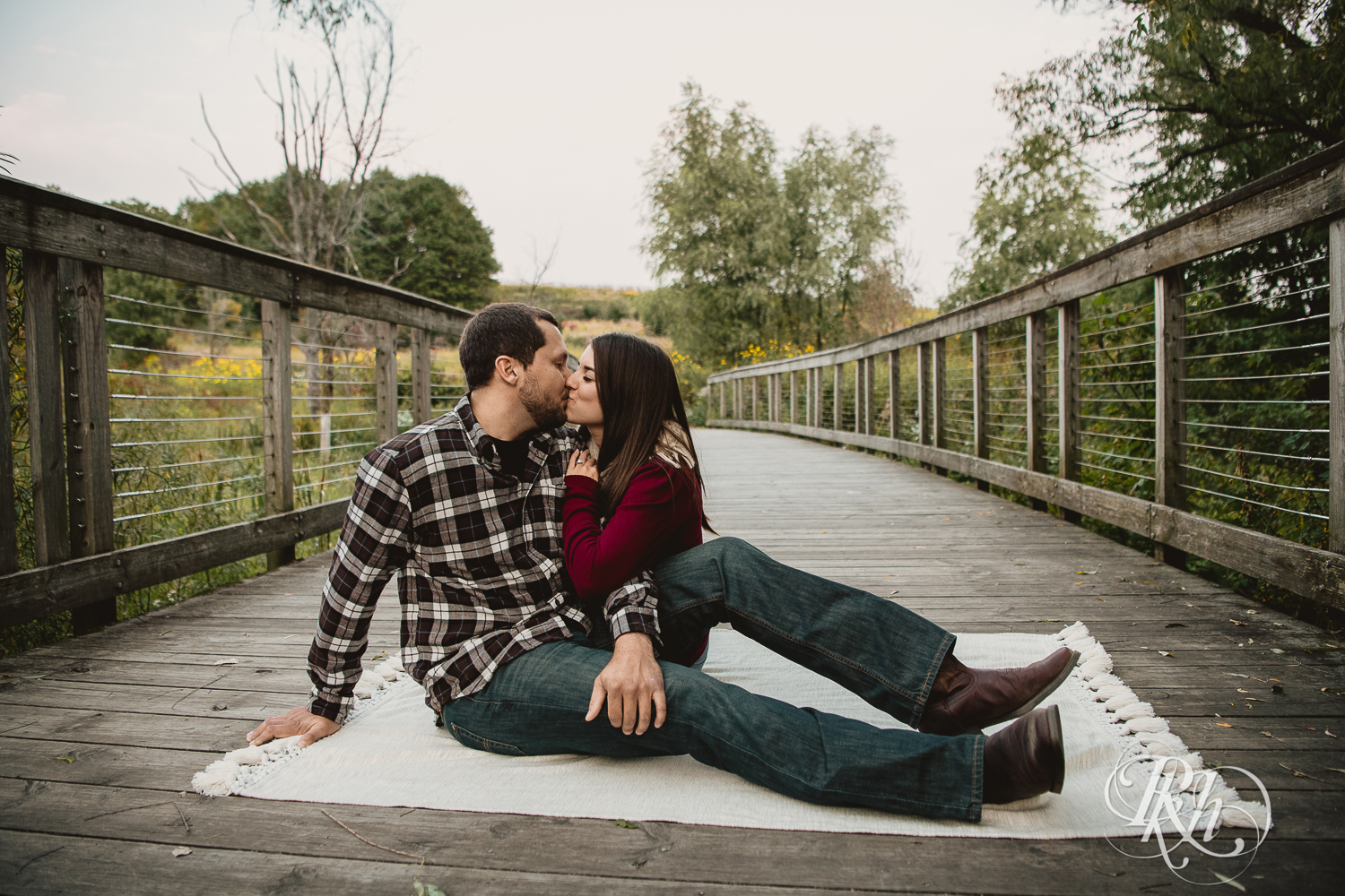 Man in flannel and woman in red shirt kiss on bridge during sunset at Lebanon Hills Regional Park in Eagan, Minnesota.