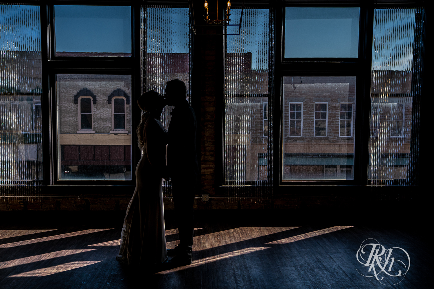 Bride and groom kiss in silhouette in front of window at the 3 Ten Event Center in Faribault, Minnesota.