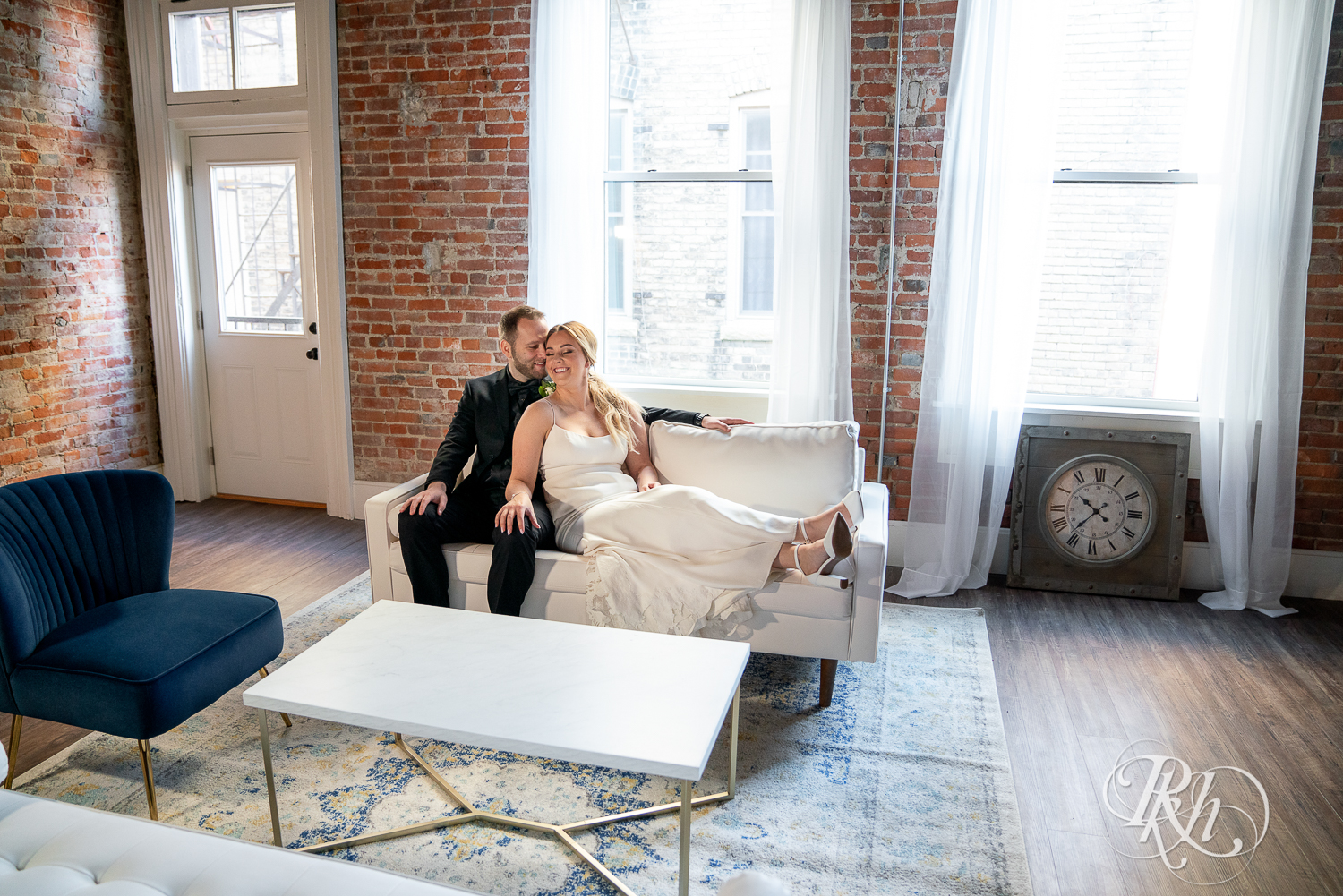 Bride and groom kiss on couch in front of window at the 3 Ten Event Center in Faribault, Minnesota.