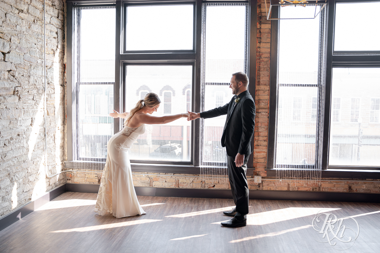 Bride and groom in black suit dance in front of a window in the 3 Ten Event Center in Faribault, Minnesota.