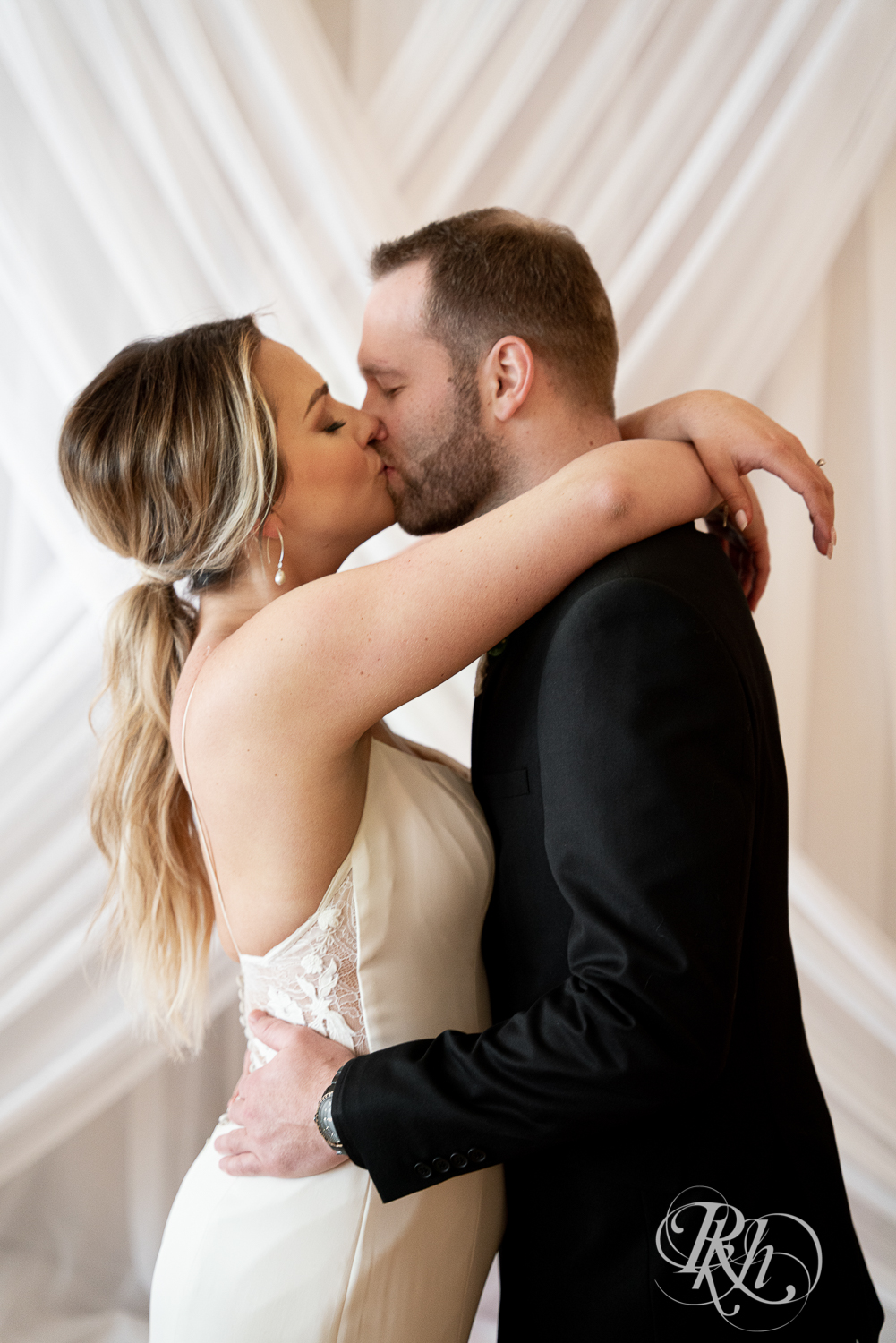 Bride and groom in black suit kiss under chandelier in the 3 Ten Event Center in Faribault, Minnesota.