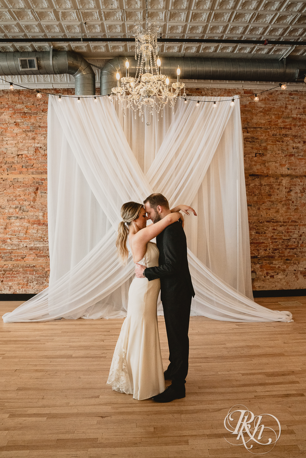 Bride and groom in black suit kiss under chandelier in the 3 Ten Event Center in Faribault, Minnesota.