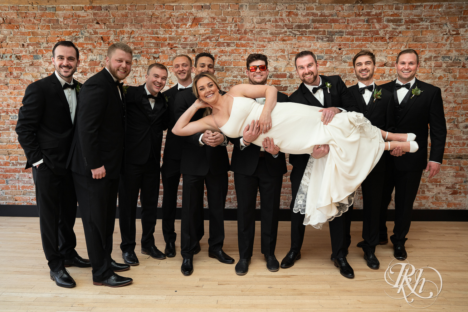 Wedding party in black suits and dresses smile at the 3 Ten Event Center in Faribault, Minnesota.
