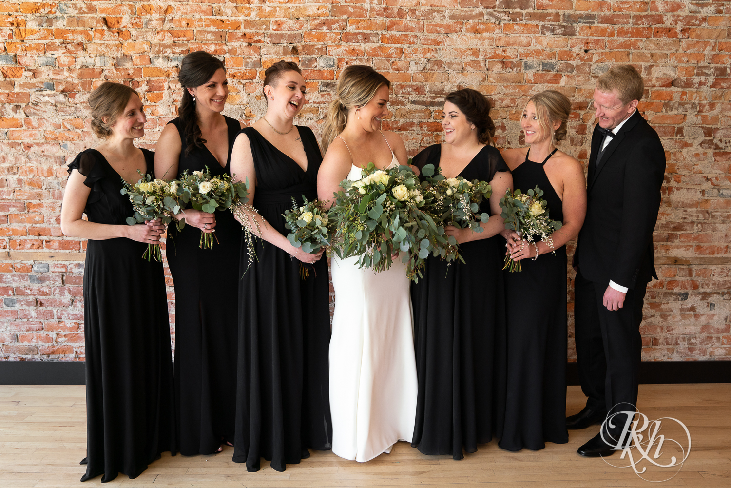 Wedding party in black suits and dresses smile at the 3 Ten Event Center in Faribault, Minnesota.