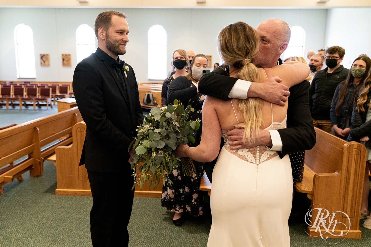Dad hugs bride at the alter in church wedding ceremony in Faribault, Minnesota.