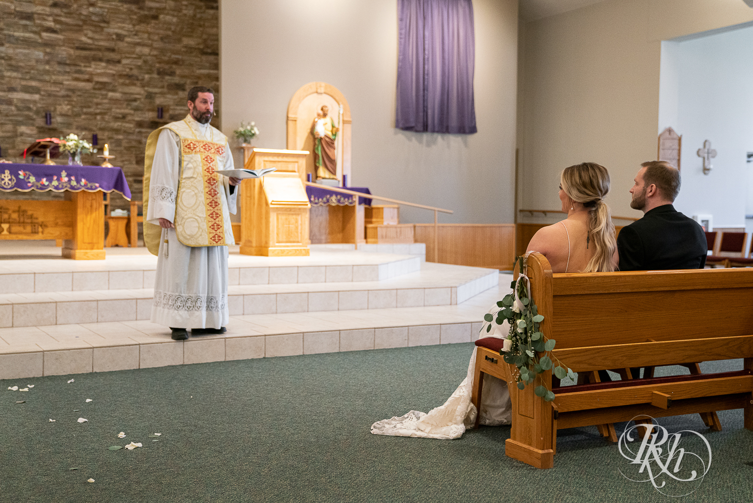 Bride and groom sit in pew in front of pastor in church wedding ceremony in Faribault, Minnesota.
