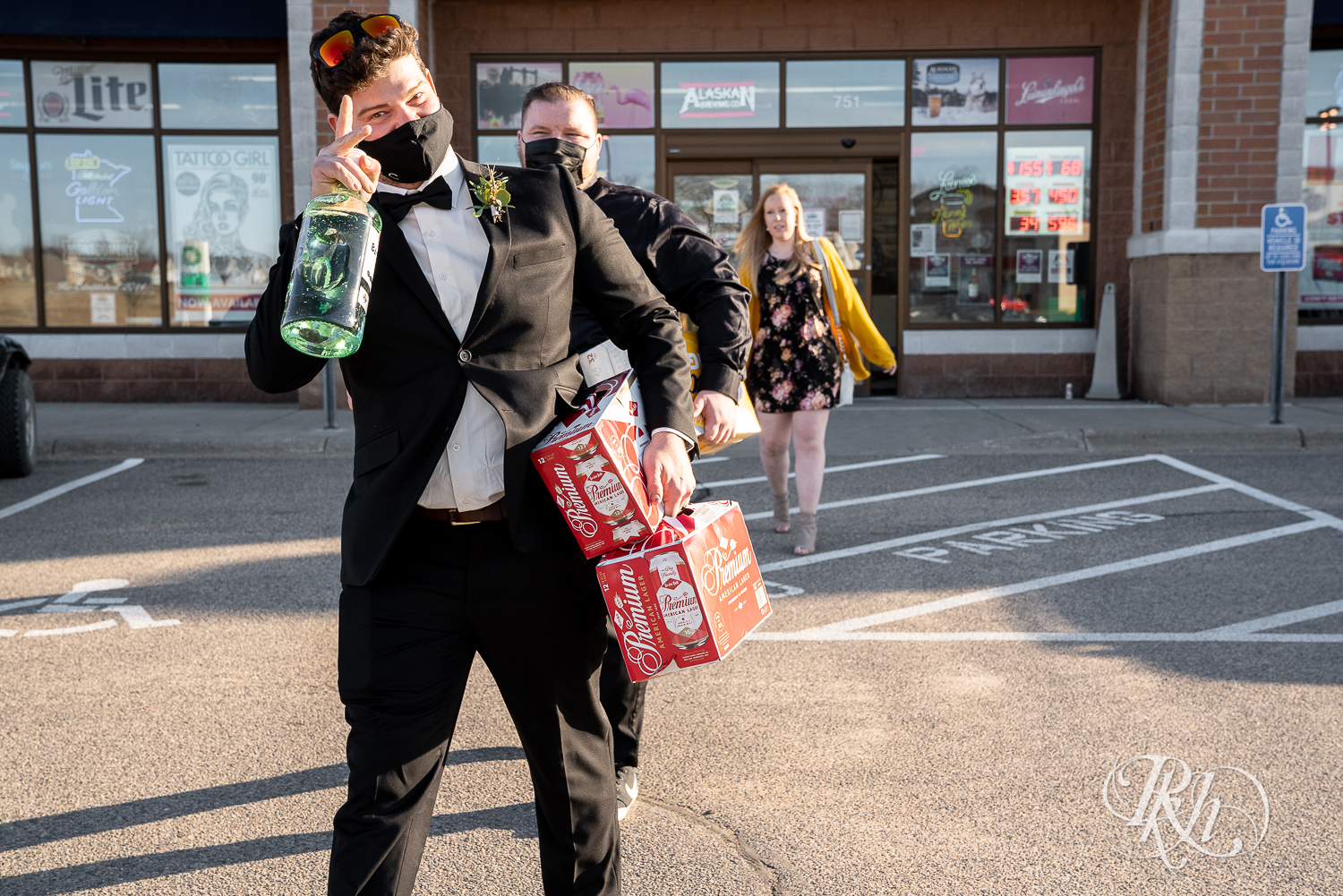 Wedding party in black suits and dresses carry bottles of alcohol out of liquor store.