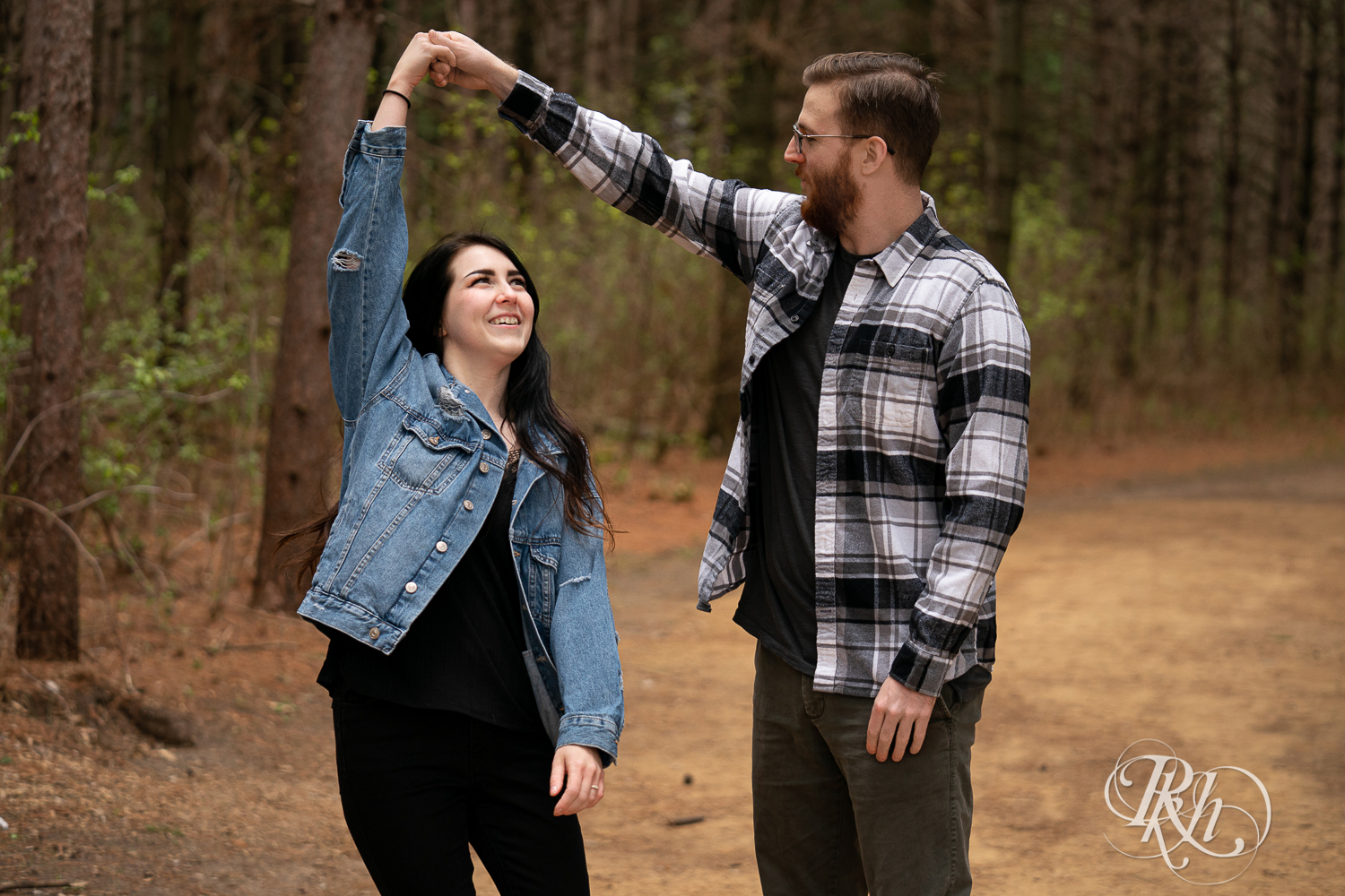 Man and woman in denim and flannel dance between trees at Lebanon Hills Regional Park in Eagan, Minnesota. 
