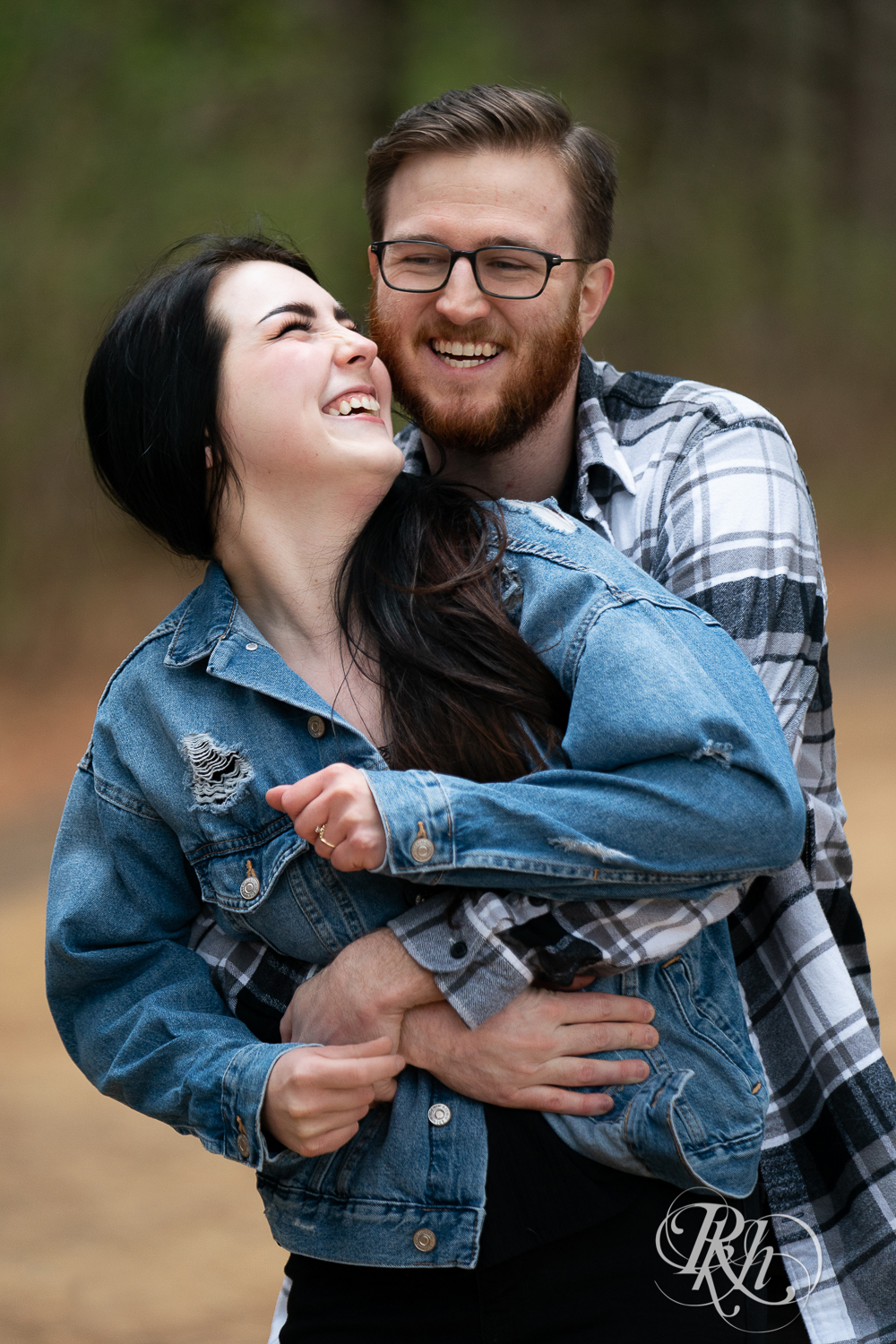 Man and woman in denim and flannel laugh between trees at Lebanon Hills Regional Park in Eagan, Minnesota. 