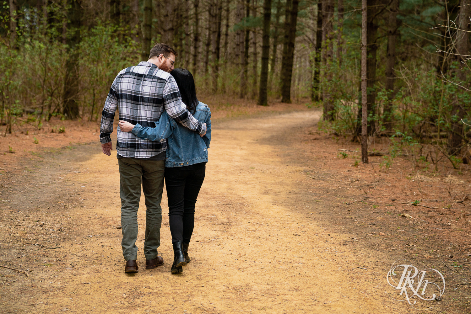 Man and woman in denim and flannel walk between trees at Lebanon Hills Regional Park in Eagan, Minnesota. 