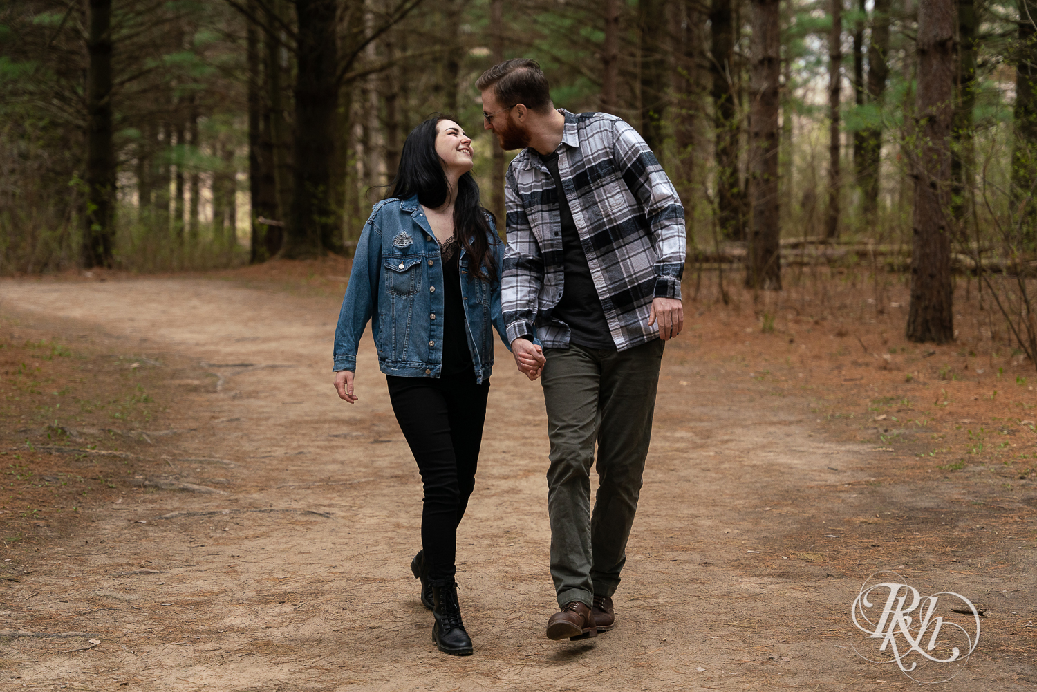 Man and woman in denim and flannel walk between trees at Lebanon Hills Regional Park in Eagan, Minnesota. 