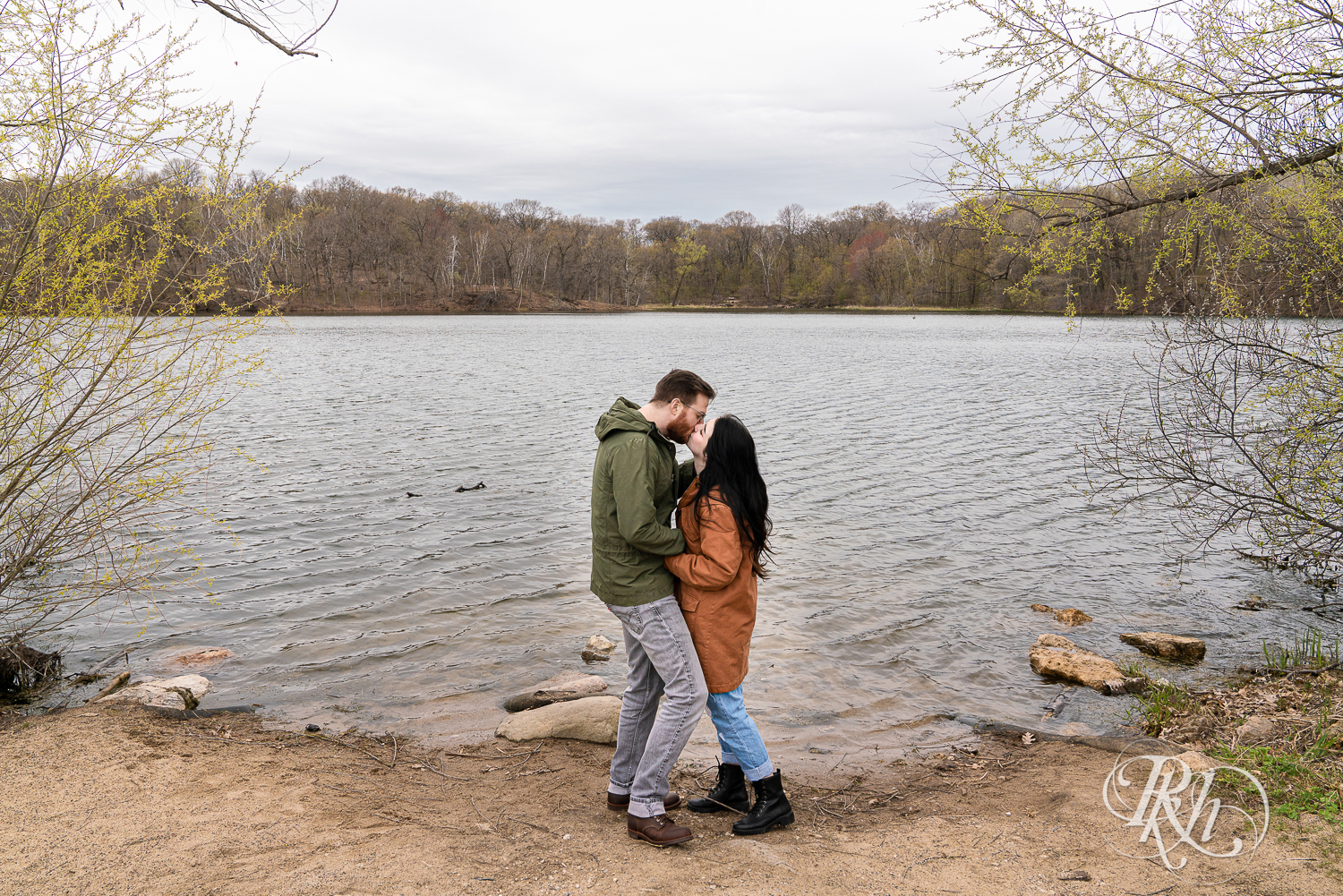 Man and woman in jackets kiss on beach at Lebanon Hills Regional Park in Eagan, Minnesota. 