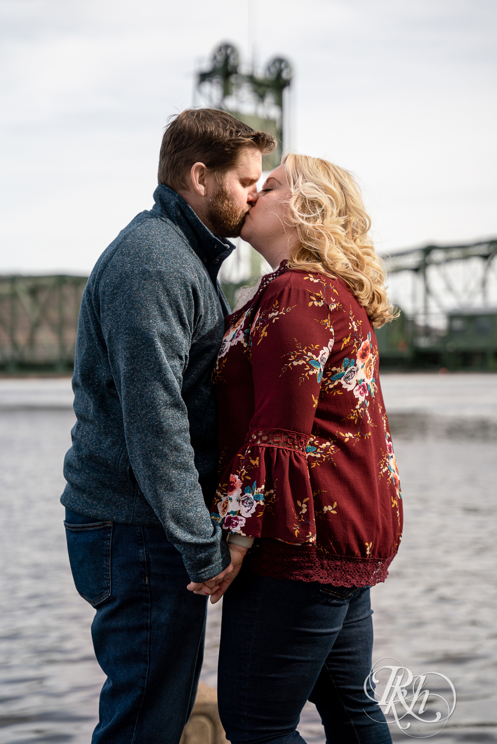 Blond woman and bearded man kiss on bridge over river in Stillwater, Minnesota.