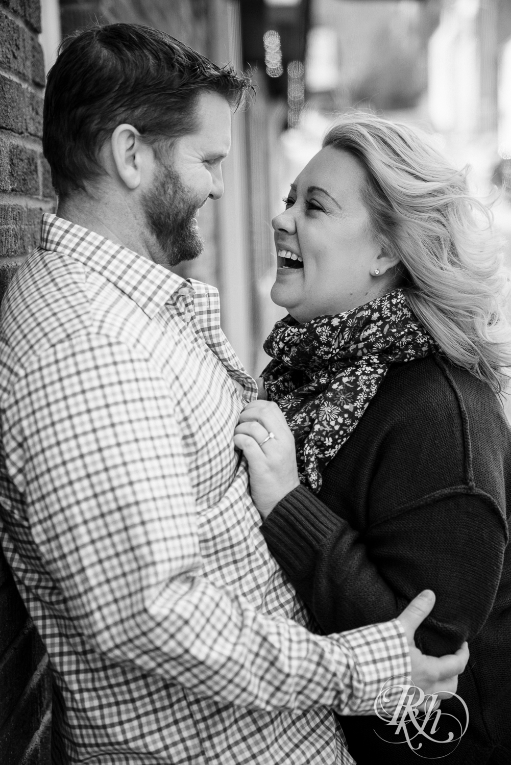 Blond woman and bearded man laugh against brick wall in Stillwater, Minnesota.