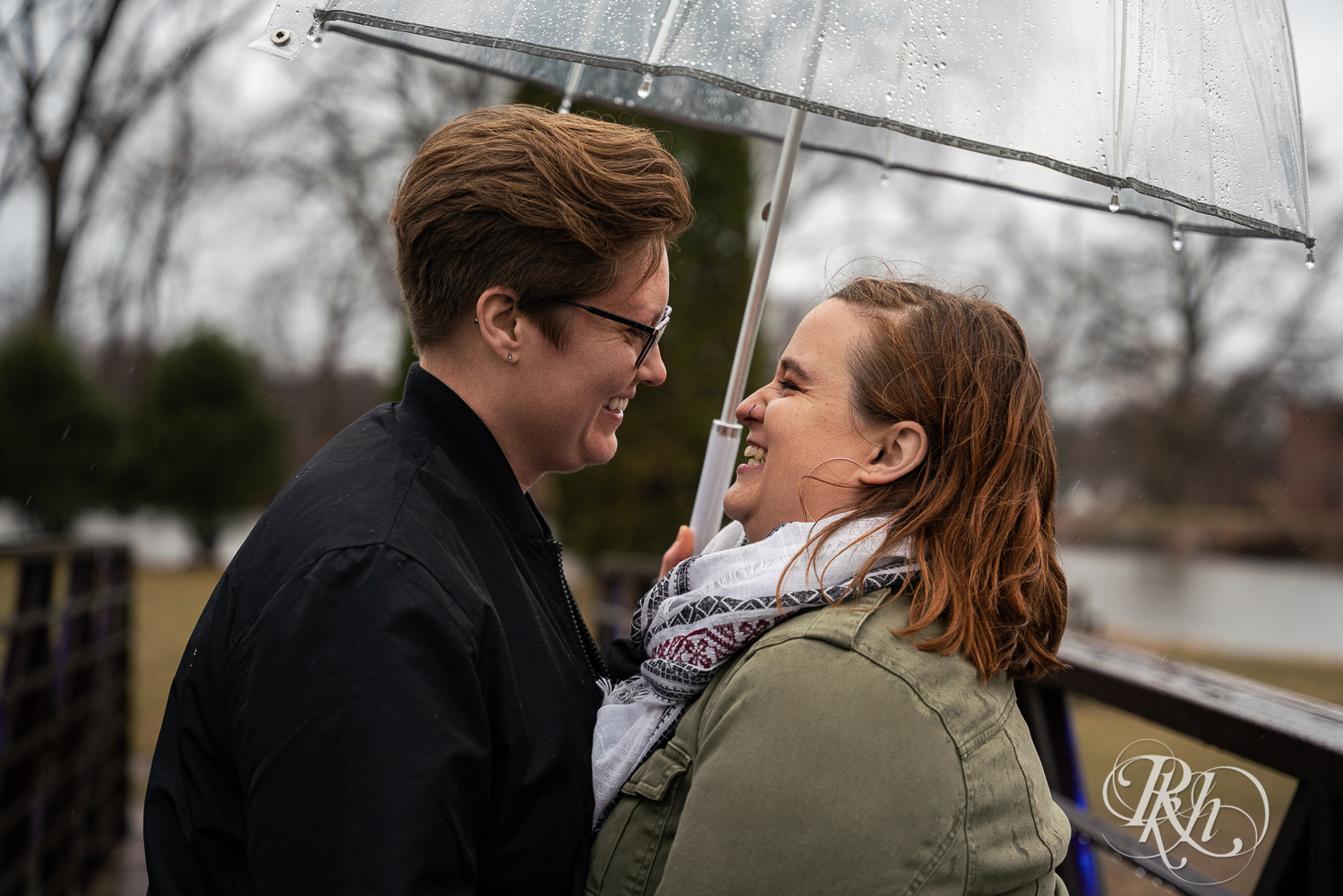 Lesbian couple smile in rain under umbrella at Saint Catherine's in Saint Paul, Minnesota. 