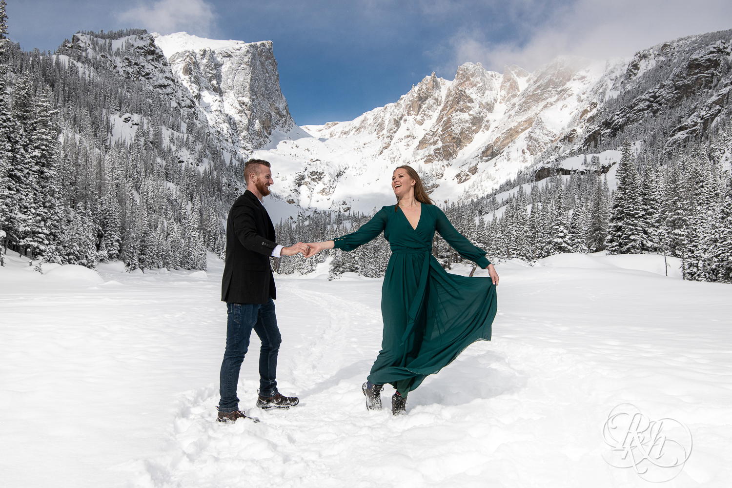 Man in suit and woman in green dress dance in snow on Dream Lake in Rocky Mountain National Park, Colorado.