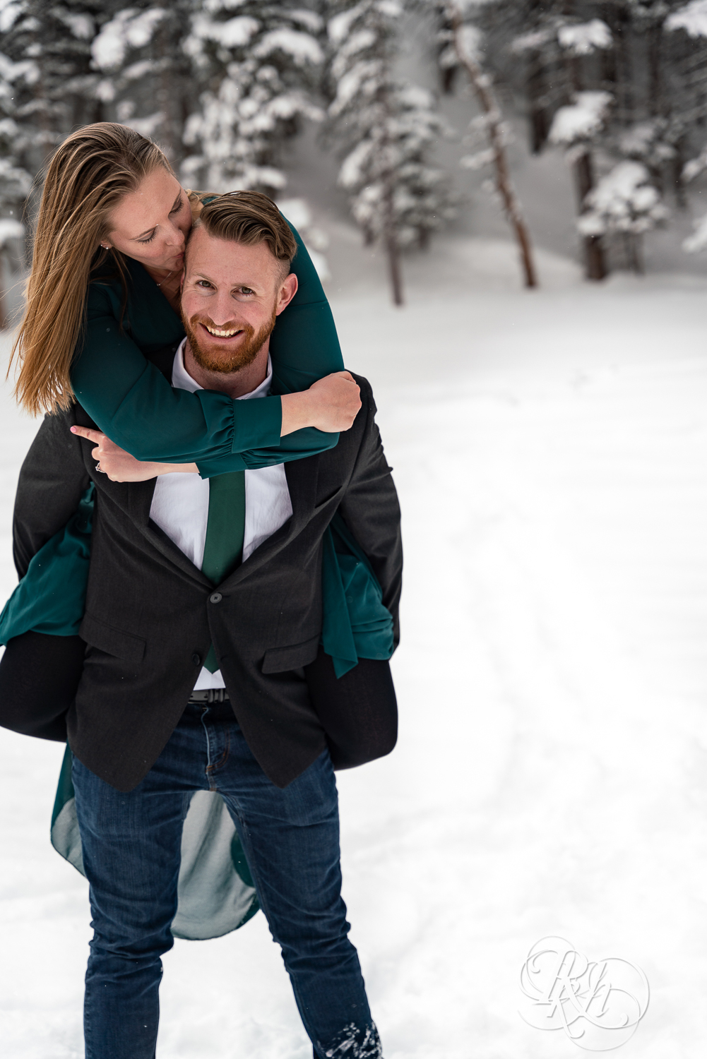 Man in suit and woman in green dress do piggy back ride in snow on Dream Lake in Rocky Mountain National Park, Colorado.