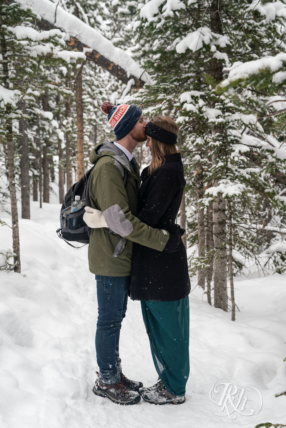 Man and woman in winter jackets and hats kiss on Rocky Mountain National Park in Colorado.