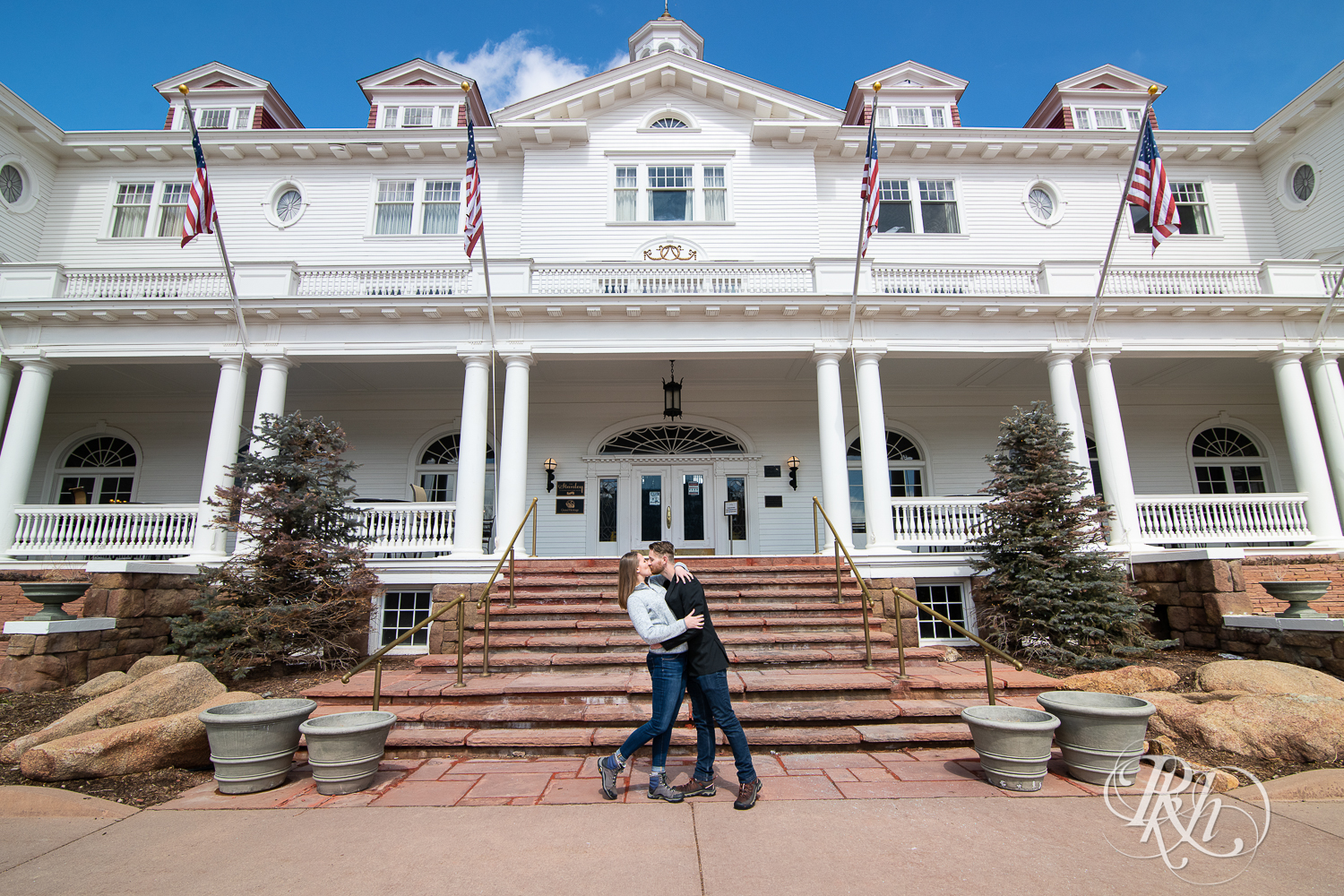 Man and woman in jeans and sweaters kiss in front of the Stanley Hotel in Estes Park, Colorado.