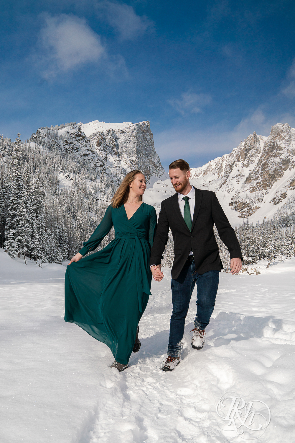 Man in suit and woman in green dress walk in snow on Dream Lake in Rocky Mountain National Park, Colorado.