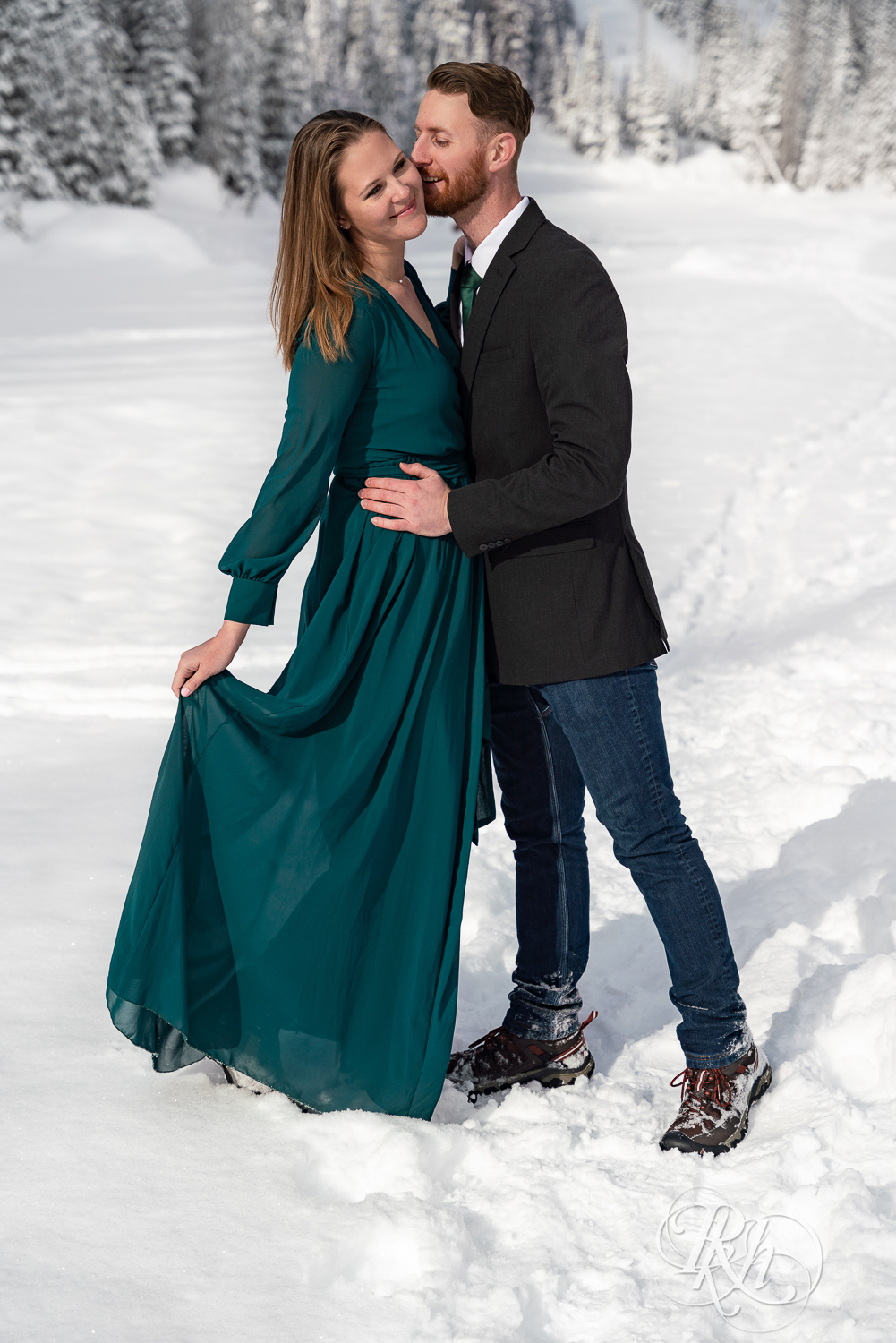 Man in suit and woman in green dress kiss in snow on Dream Lake in Rocky Mountain National Park, Colorado.