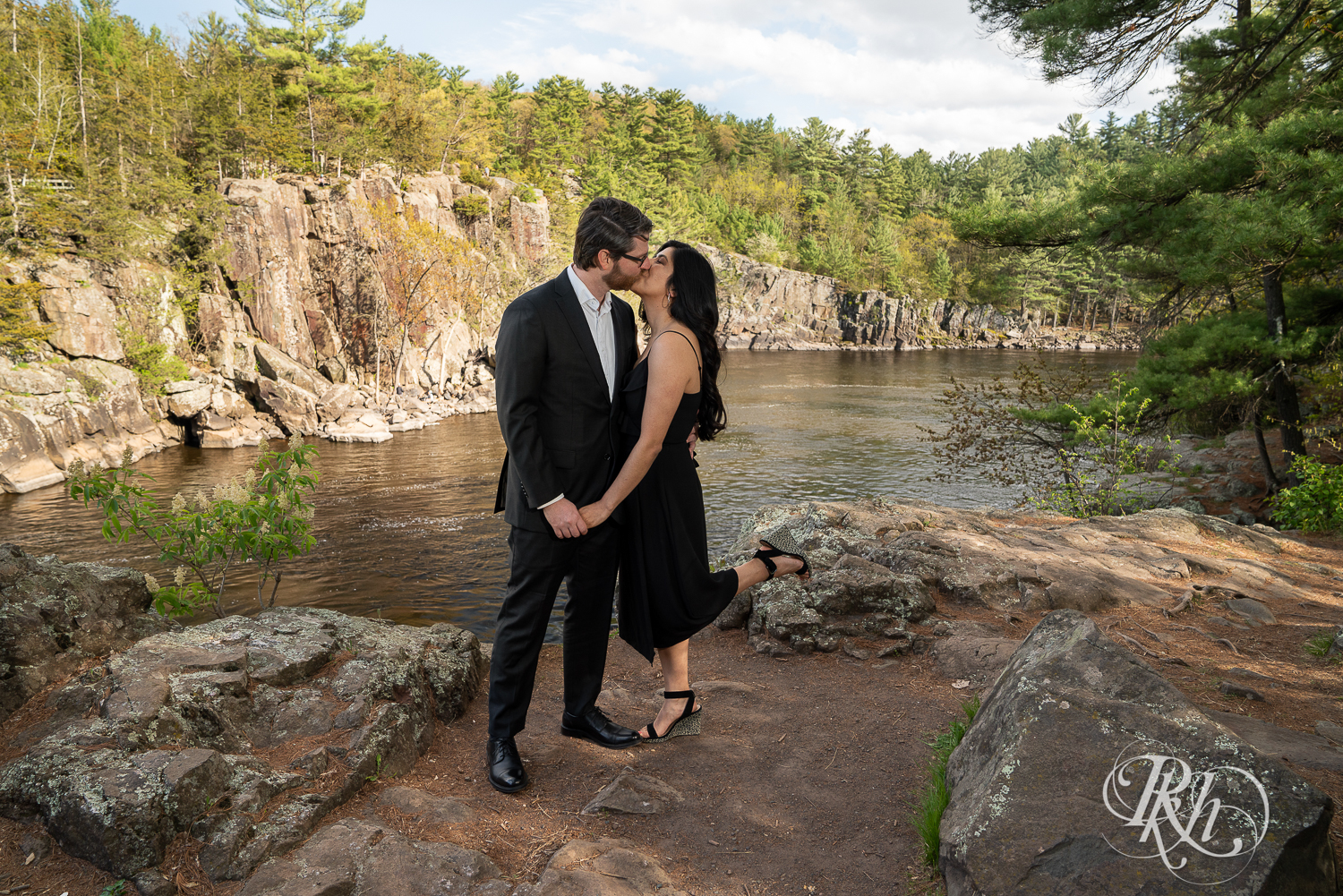 Man in suit and woman in long black dress kiss on cliff at Interstate State Park in Taylor's Fall, Minnesota.