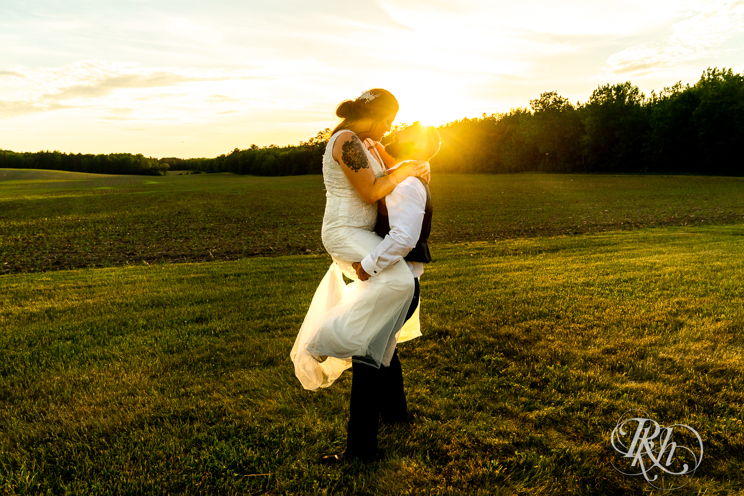 Groom lifts bride in field during sunset at wedding at Pine Peaks Event Center in Pine River, Minnesota.