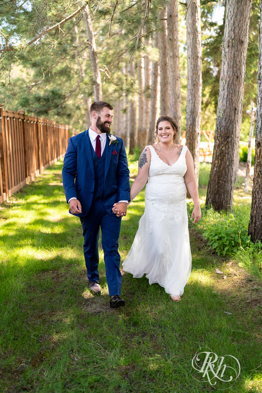 Bride and groom walk between pine trees at Pine Peaks Event Center in Pine River, Minnesota.