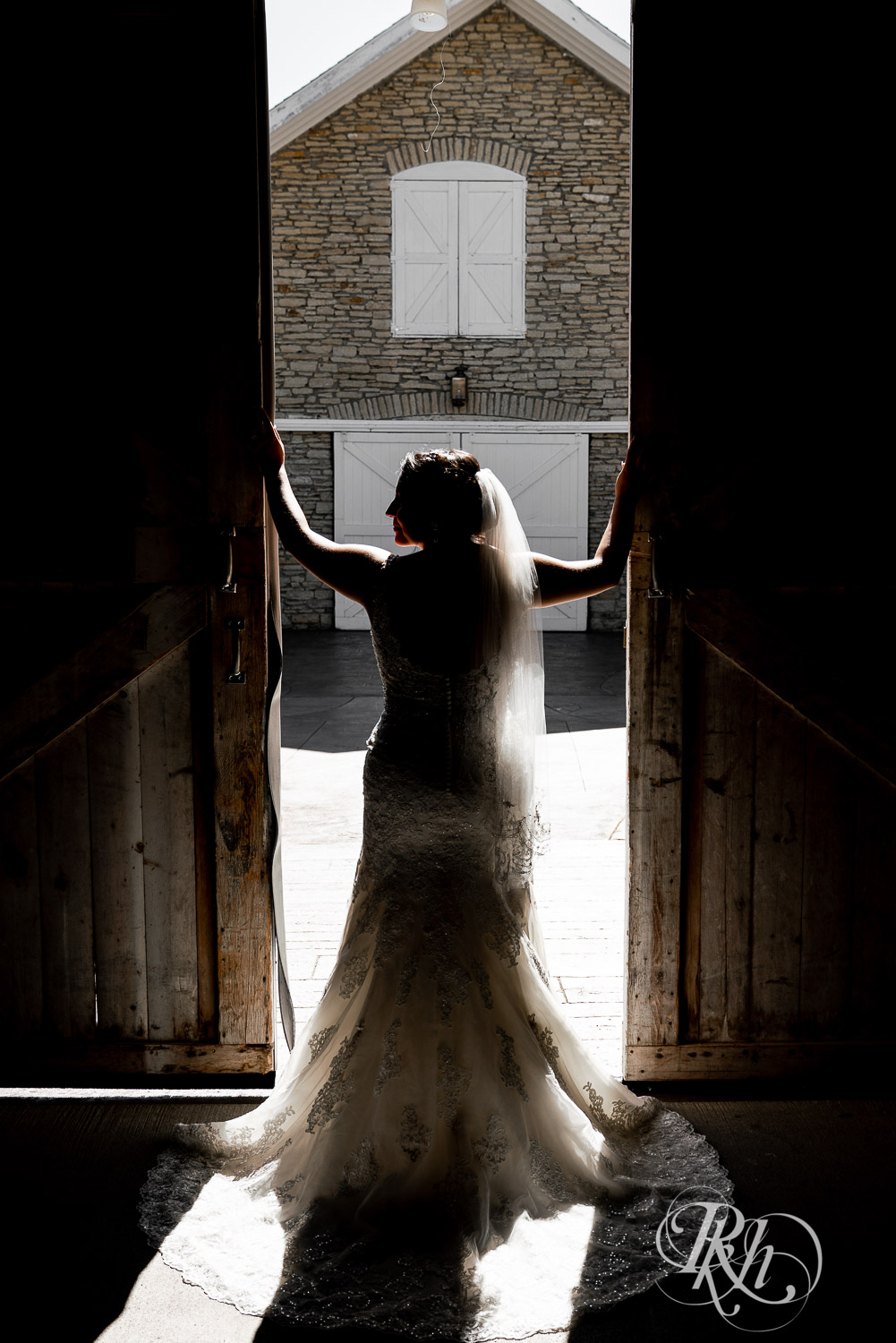 Bride standing in silhouette between barn doors at summer brunch wedding at Mayowood Stone Barn in Rochester, Minnesota.