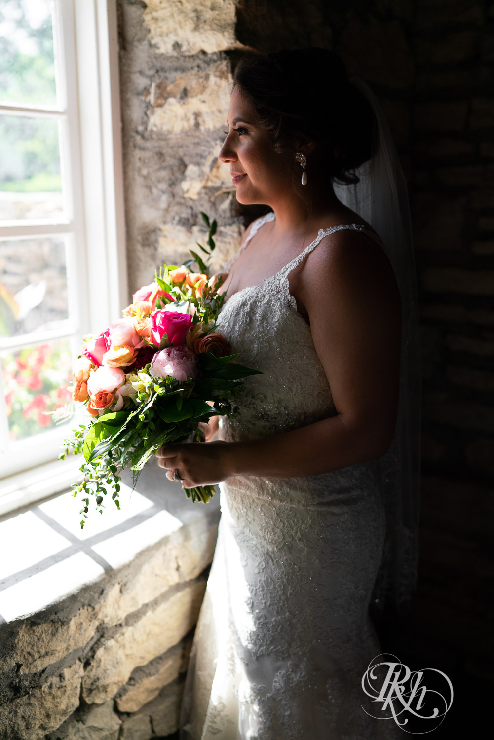 Bride holding flowers looking out the window at summer brunch wedding at Mayowood Stone Barn in Rochester, Minnesota.