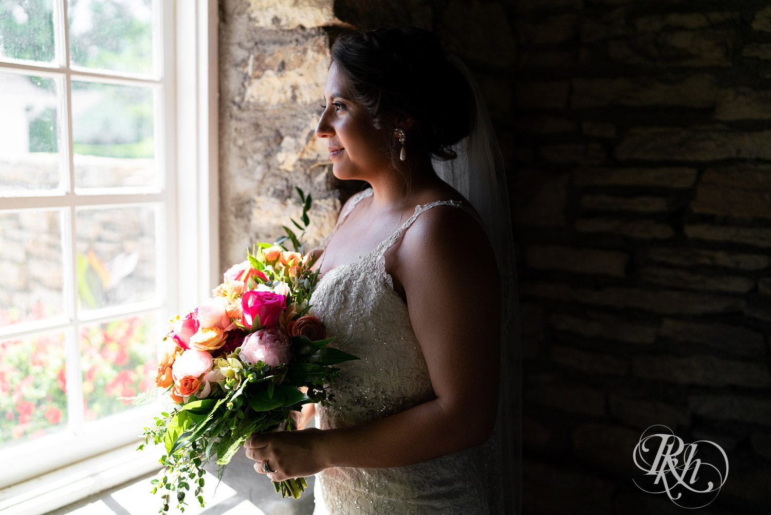 Bride holding flowers looking out the window at summer brunch wedding at Mayowood Stone Barn in Rochester, Minnesota.