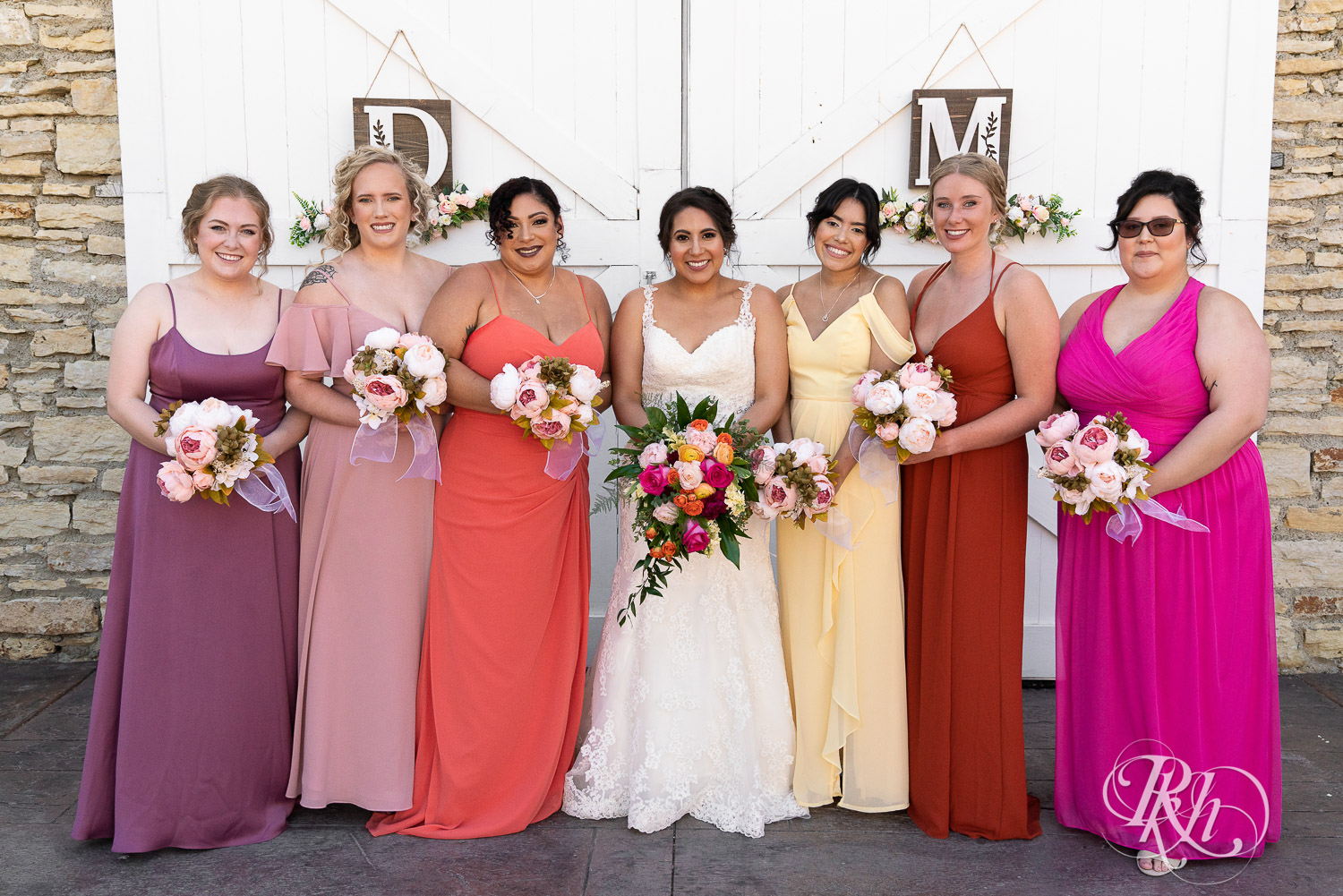 Wedding party in different colored dresses smiling at summer wedding at Mayowood Stone Barn in Rochester, Minnesota.