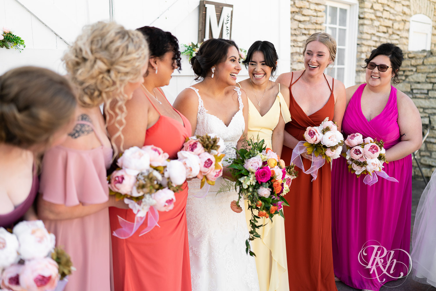 Wedding party in different colored dresses laughing at summer wedding at Mayowood Stone Barn in Rochester, Minnesota.
