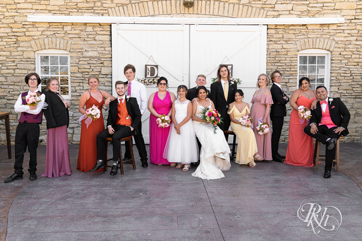 Wedding party in different colored dresses laughing at summer wedding at Mayowood Stone Barn in Rochester, Minnesota.
