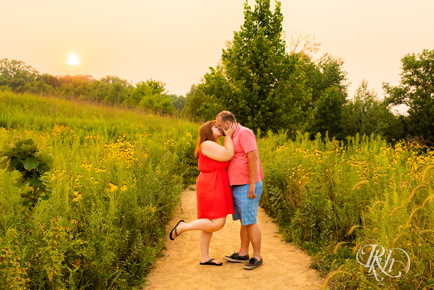 Man and women in orange dress kiss in flowers at sunset at Lebanon Hills Regional Park in Eagan, Minnesota.