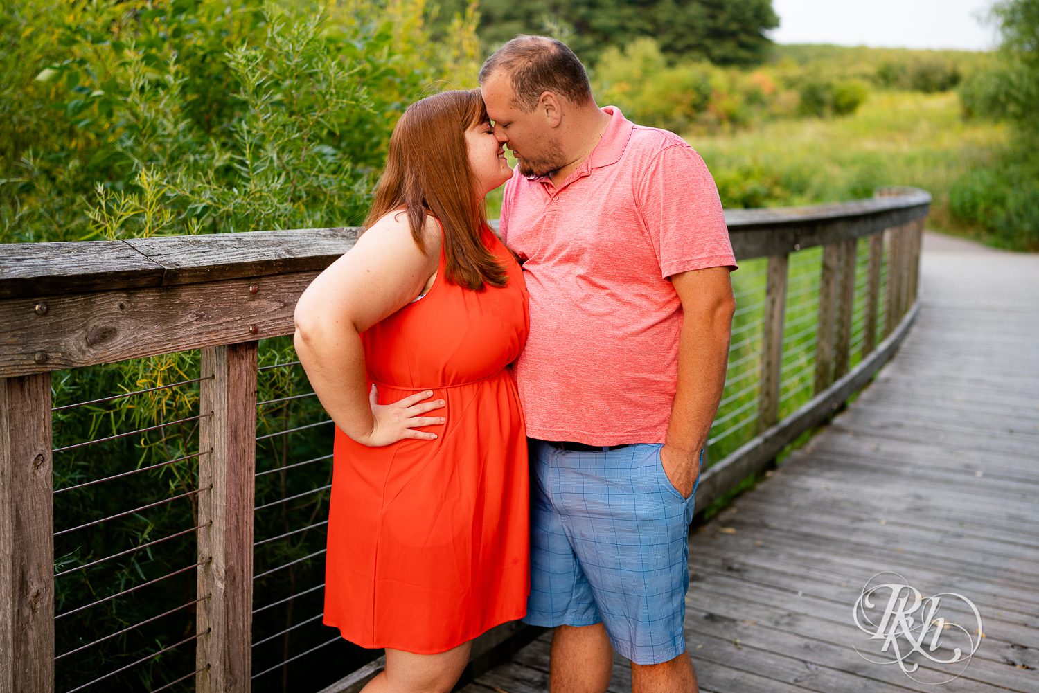 Man and women in orange dress kiss on bridge at Lebanon Hills Regional Park in Eagan, Minnesota.