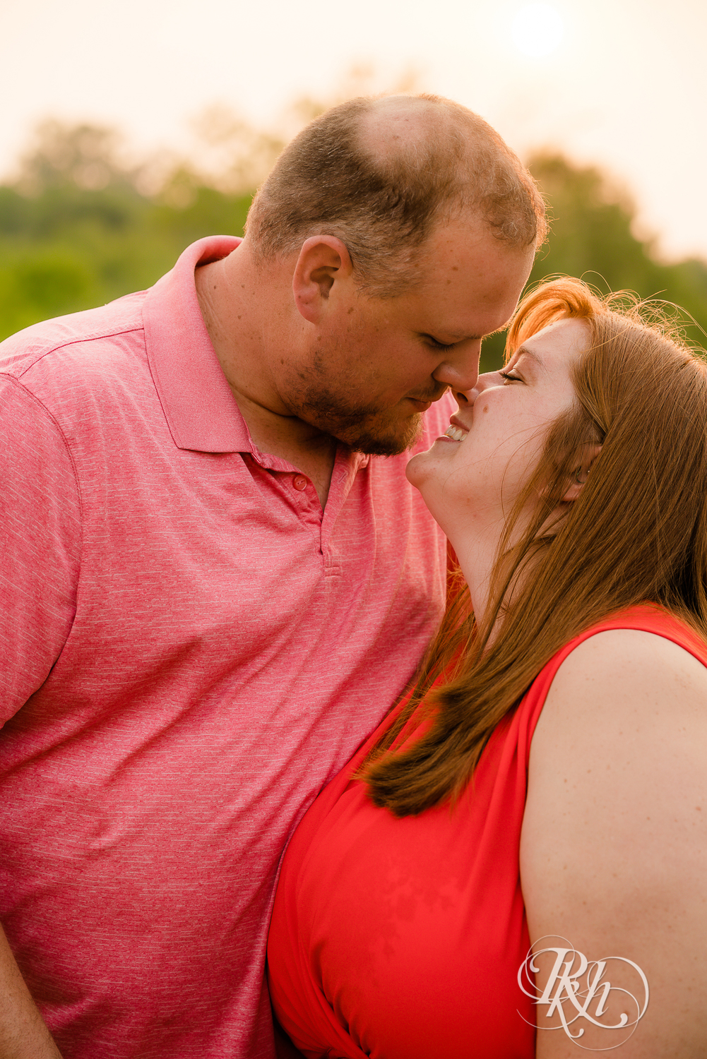 Man and women in orange dress kiss at sunset at Lebanon Hills Regional Park in Eagan, Minnesota.