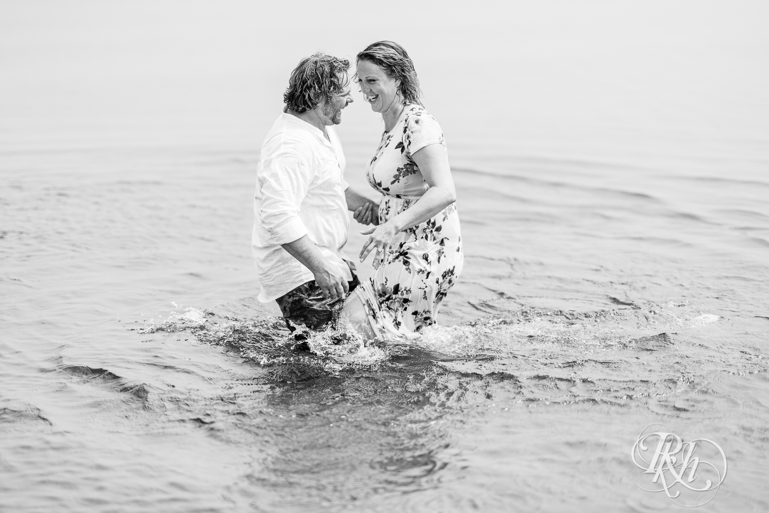 Man and woman splash water at each other in Lake Superior during engagement photos on Park Point Beach in Duluth, Minnesota.