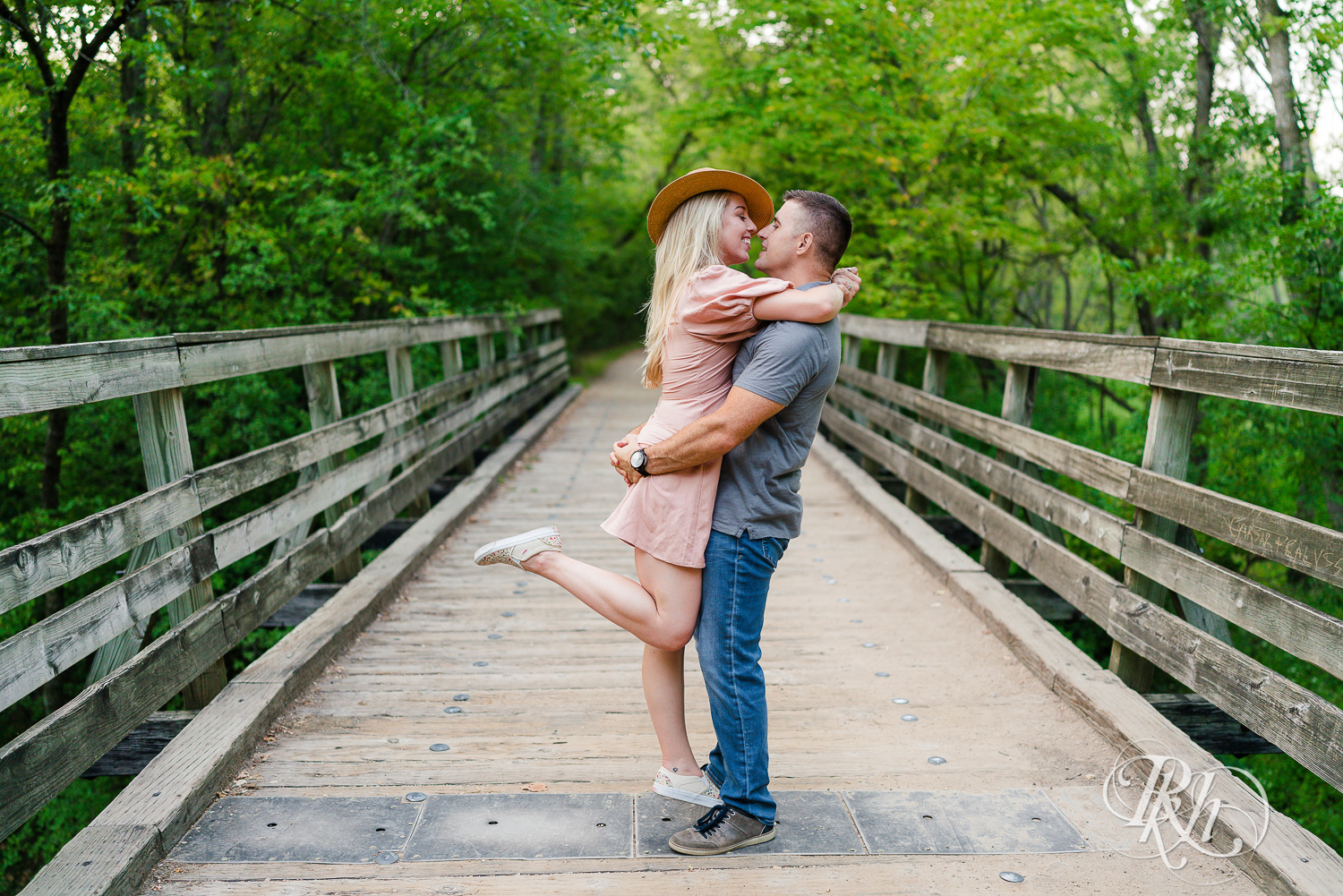Man lifts blonde woman in hat and dress on a bridge at Afton State Park in Hastings, Minnesota.