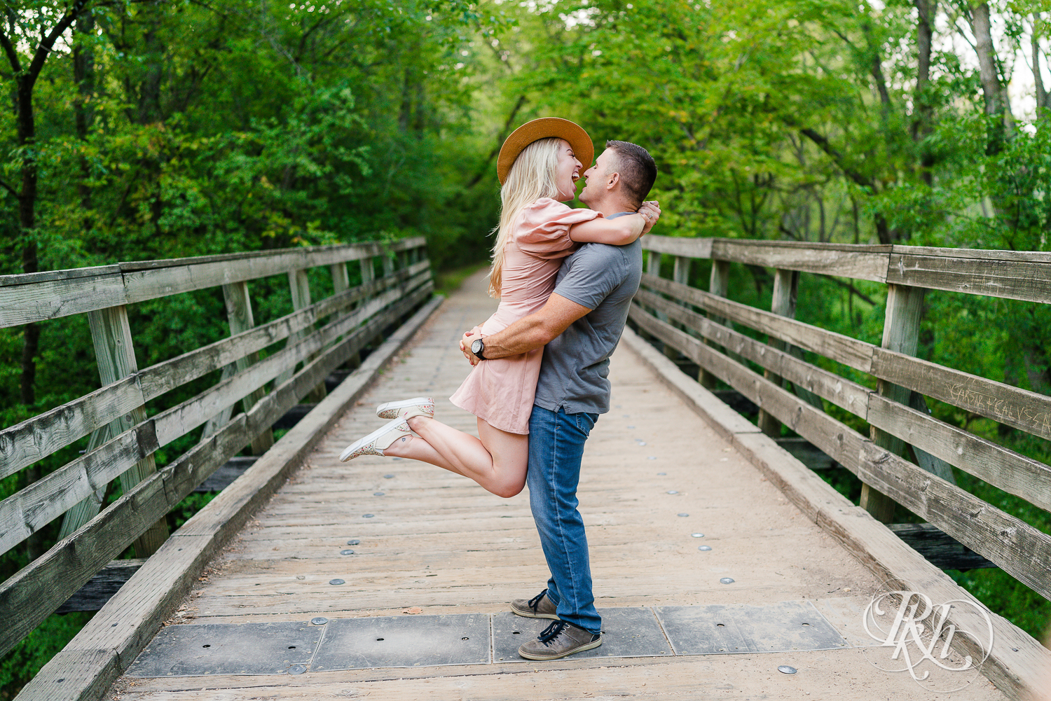 Man lifts blonde woman in hat and dress on a bridge at Afton State Park in Hastings, Minnesota.
