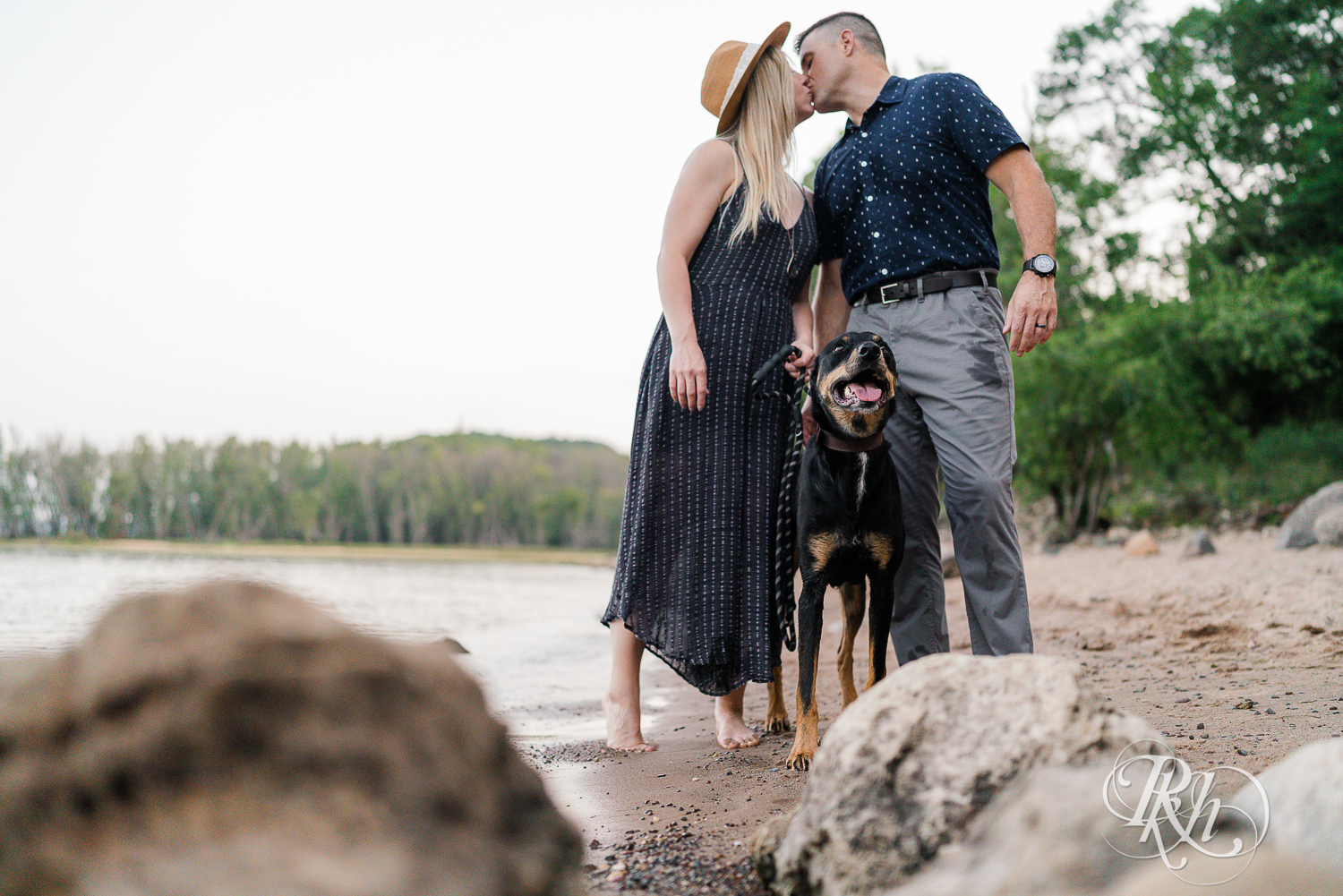 Man and woman in blue dress kiss behind their Doberman on beach at Afton State Park in Hastings, Minnesota.