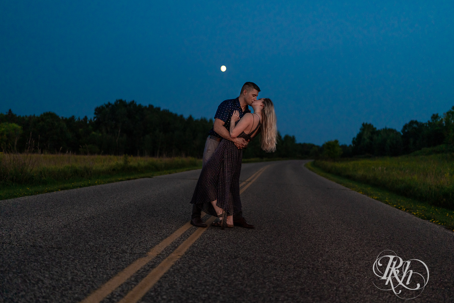 Man and woman kiss in front of the moon in the middle of the road at Afton State Park in Hastings, Minnesota.