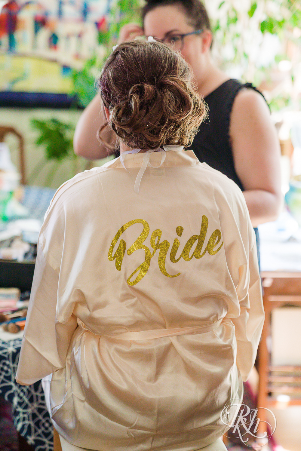 Bride getting makeup done while wearing a robe that has Bride written on the back.