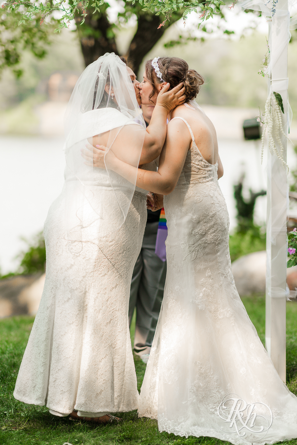Lesbian brides kiss during outdoor wedding ceremony in Minnesota.