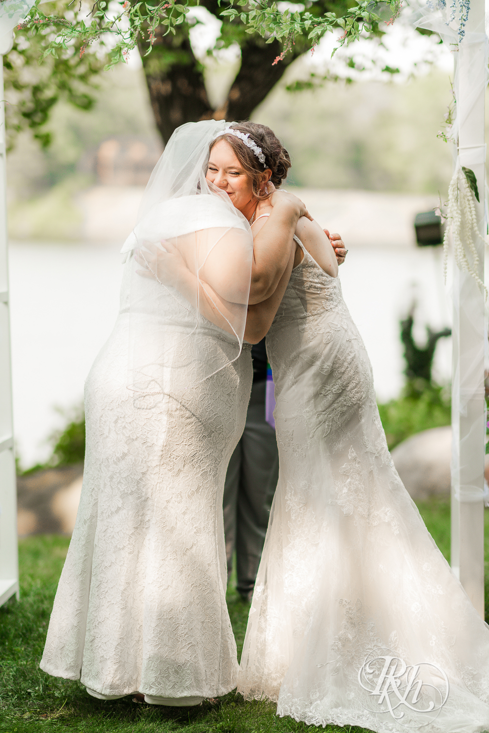 Lesbian brides hug during outdoor wedding ceremony in Minnesota.