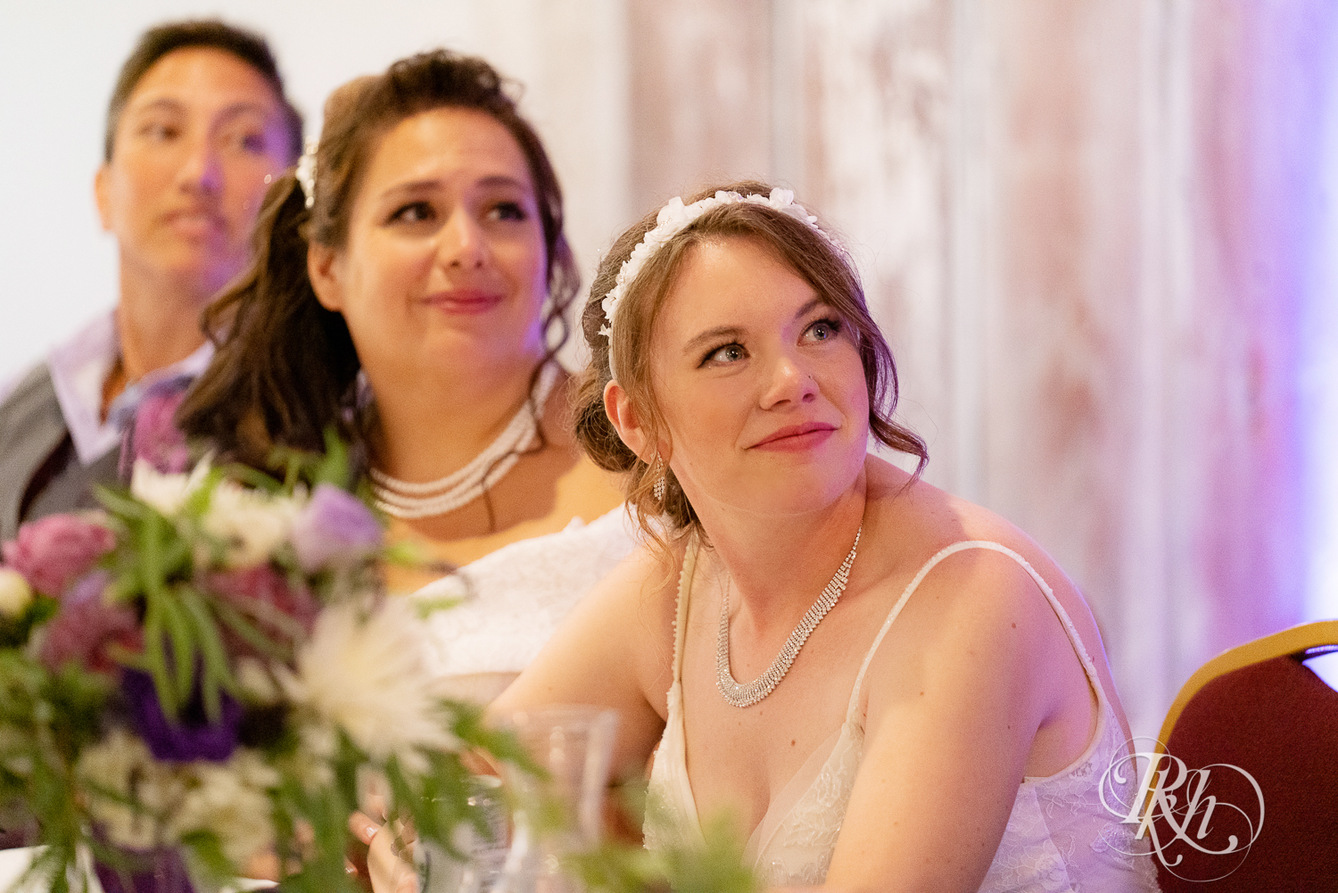 Lesbian brides smile at head table at wedding reception at Willy McCoy's in Champlin, Minnesota.